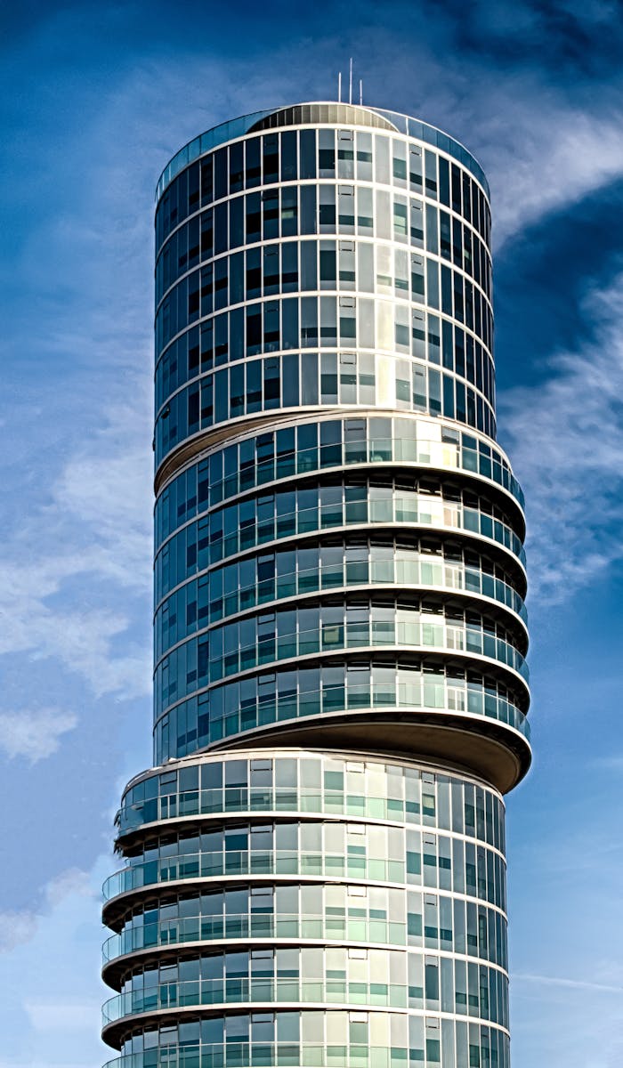 Low angle view of a modern glass skyscraper against a blue sky, showcasing futuristic architecture.